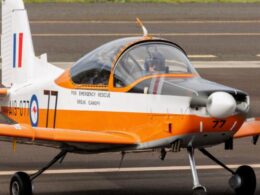 Orange and white rescue aircraft on tarmac with canopy closed text on fuselage reads FOR EMERGENCY RESCUE BREAK CANOPY and tail number 77