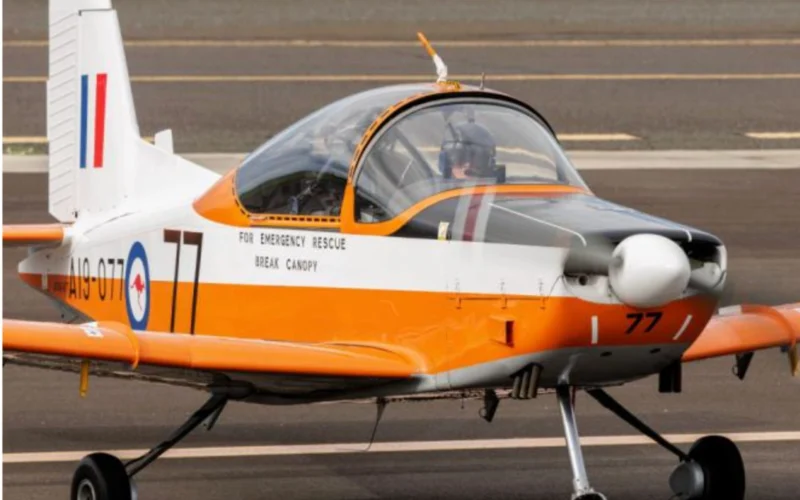 Orange and white rescue aircraft on tarmac with canopy closed text on fuselage reads FOR EMERGENCY RESCUE BREAK CANOPY and tail number 77