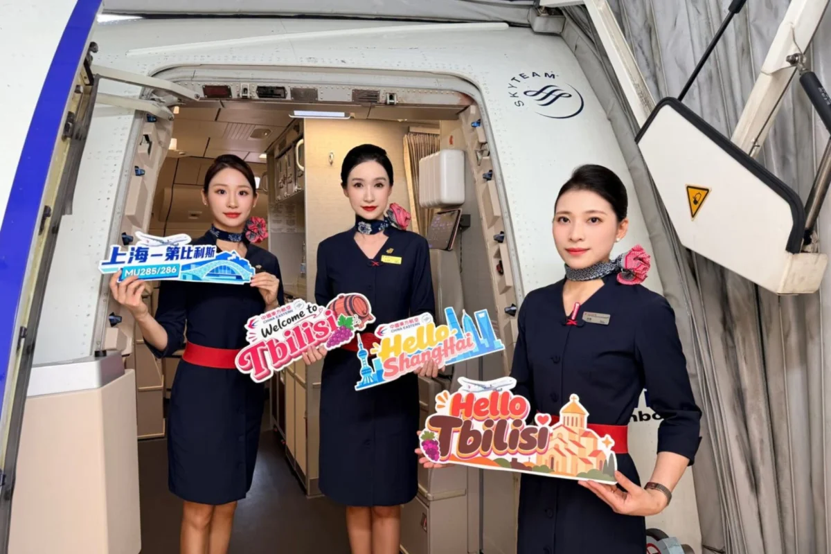 China Eastern launches direct Shanghai Tbilisi flight Three flight attendants in navy uniforms stand in an airplane doorway holding colorful welcome signs Hello Tbilisi Hello Shanghai