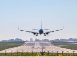 Front view of a blue passenger jet landing on a runway with a city skyline in the distance