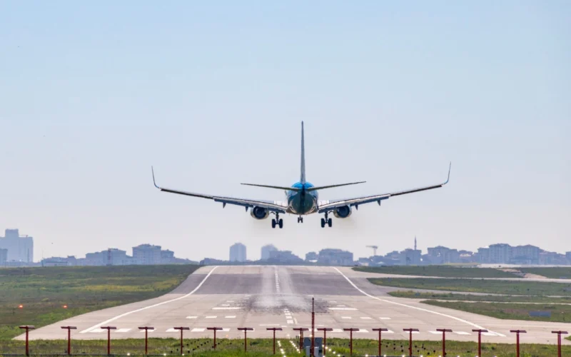 Front view of a blue passenger jet landing on a runway with a city skyline in the distance