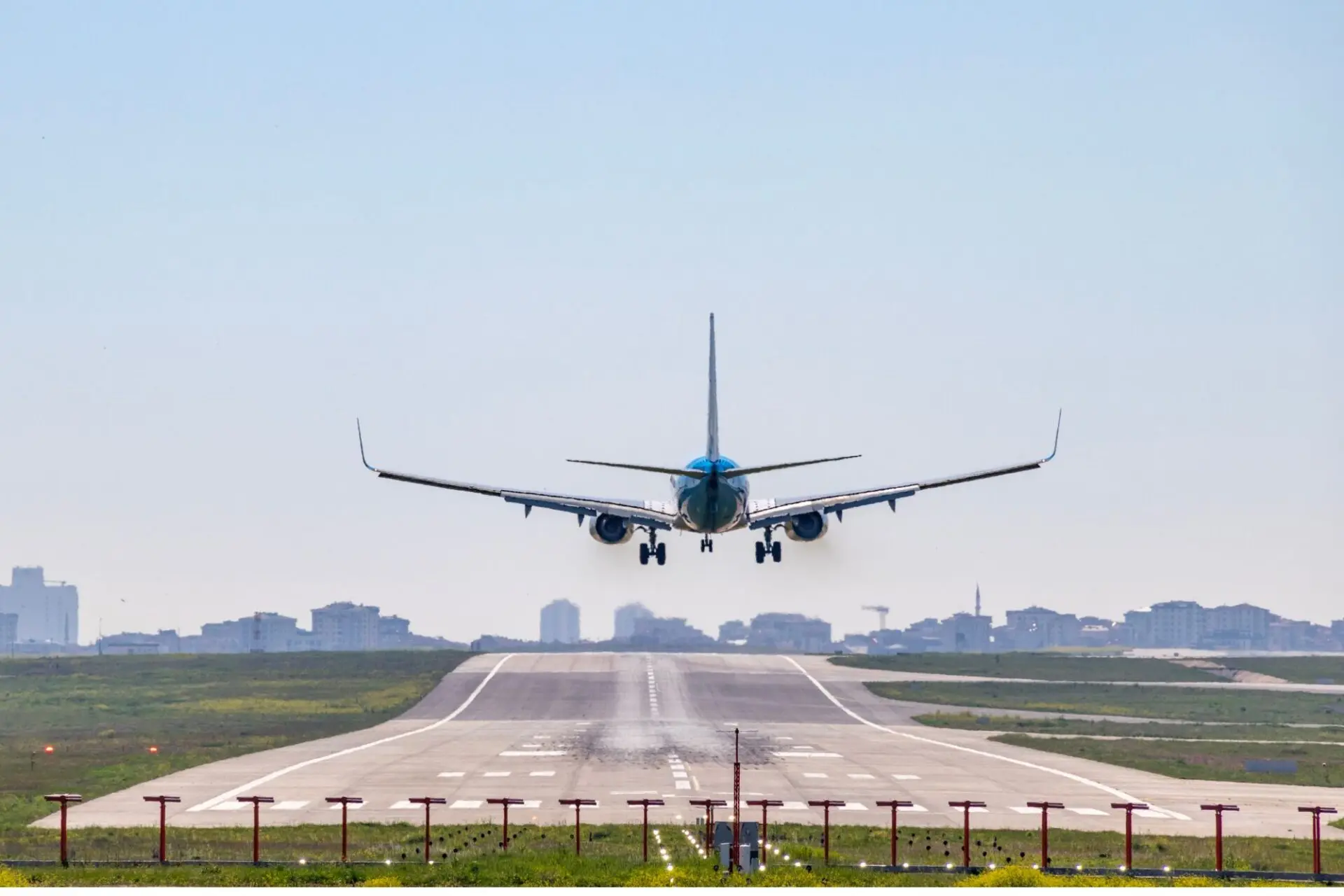 Front view of a blue passenger jet landing on a runway with a city skyline in the distance