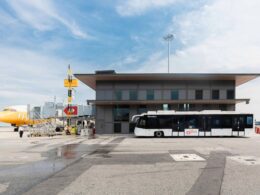 Airport tarmac with a yellow airplane at the gate a modern gray terminal building and a white bus in front