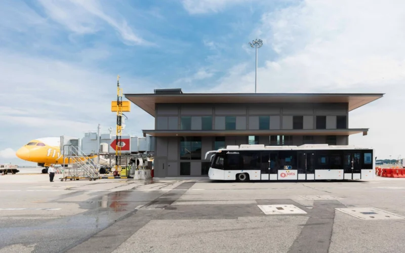 Airport tarmac with a yellow airplane at the gate a modern gray terminal building and a white bus in front