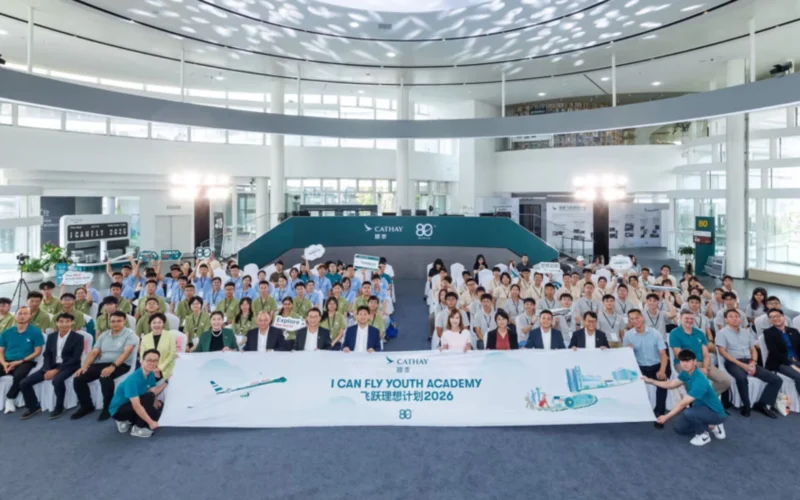 Large crowd of people in a bright atrium pose for a group photo behind a banner that reads I CAN FLY YOUTH ACADEMY with Cathay logos in the background