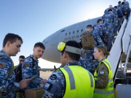 Group of uniformed air force personnel boarding a large military aircraft via mobile stairs guided by a crew member in a high visibility vest