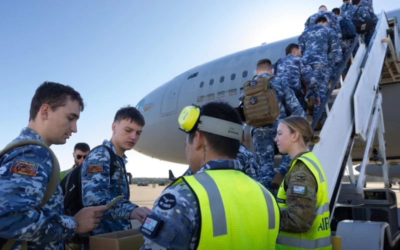 Group of uniformed air force personnel boarding a large military aircraft via mobile stairs guided by a crew member in a high visibility vest
