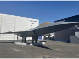 Large aircraft wing mounted on pedestals at an outdoor exhibition with white walls and Textron signage in the background under a blue sky