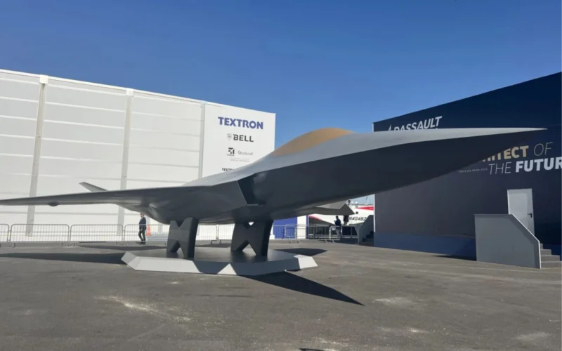 Large aircraft wing mounted on pedestals at an outdoor exhibition with white walls and Textron signage in the background under a blue sky
