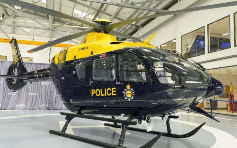 Yellow and navy police helicopter on display inside a hangar with rotor blades extended