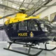 Yellow and navy police helicopter on display inside a hangar with rotor blades extended