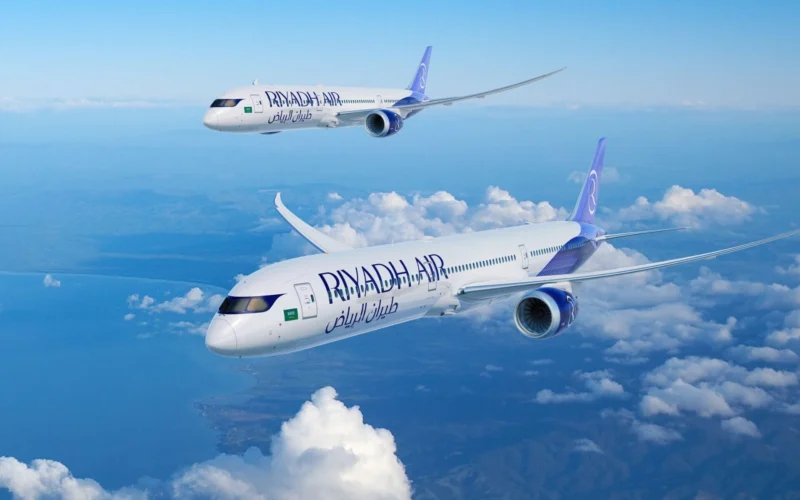 Two Ryanair airplanes in flight over a sea of white clouds against a bright blue sky one closer to the viewer and another farther away in formation