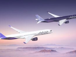 Two Riyadh Air airplanes in purple and white livery fly in formation over a purple pink sunset over a mountainous horizon tails branded with the airline logo