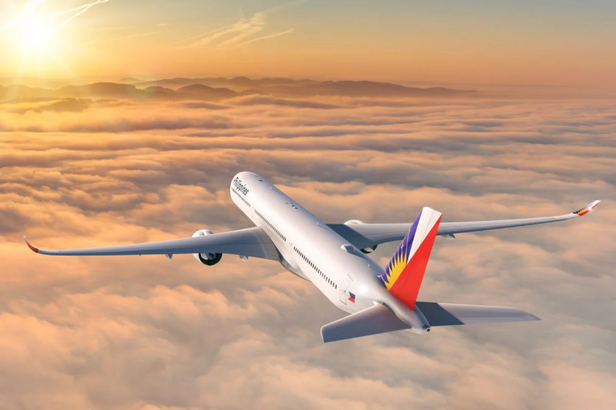 Commercial passenger jet in flight above orange clouds at sunset tail painted with a Philippine flag design