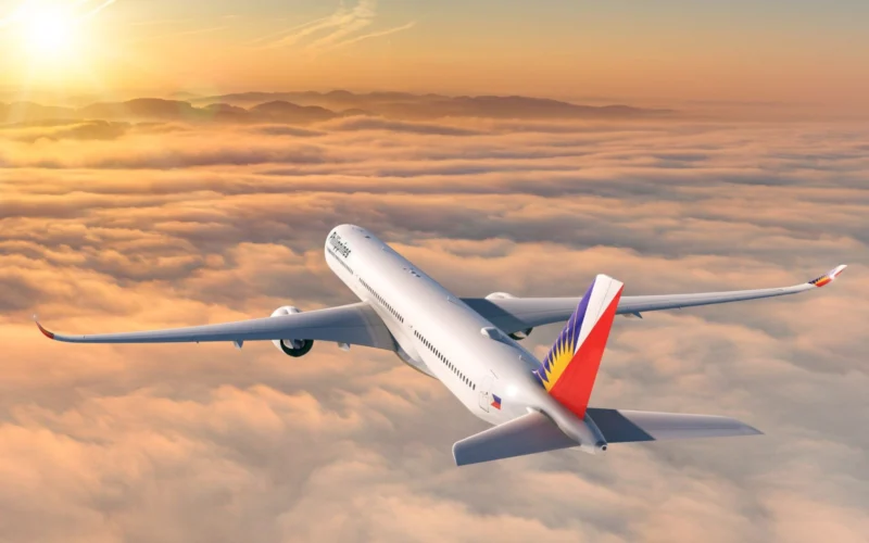 Commercial passenger jet in flight above orange clouds at sunset tail painted with a Philippine flag design