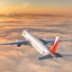 Commercial passenger jet in flight above orange clouds at sunset tail painted with a Philippine flag design