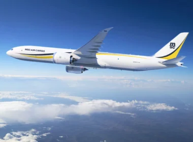 White MSC Air Cargo Boeing 777 freighter flying above clouds against a blue sky, yellow and black tail logo visible