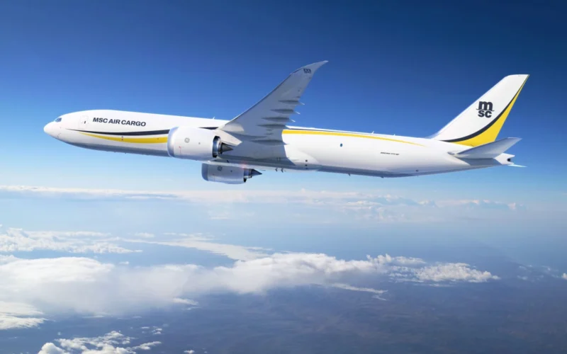 White MSC Air Cargo Boeing 777 freighter flying above clouds against a blue sky yellow and black tail logo visible