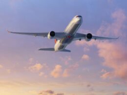Commercial airliner photographed from below as it soars through a pastel sunset sky engines visible under the wings with a colorful tail