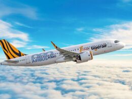 Airbus A320 jet with tiger stripe tail livery flying above a cloudy blue sky