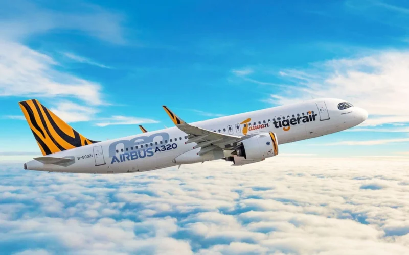 Airbus A320 jet with tiger stripe tail livery flying above a cloudy blue sky