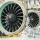 Two large jet engine nacelles suspended in a maintenance hangar showing turbine blades in view
