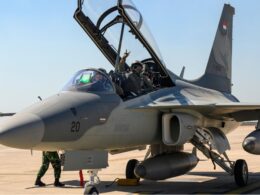 Two pilots in an open cockpit of a fighter jet on a desert airstrip ground crew nearby preparing for taxiflight