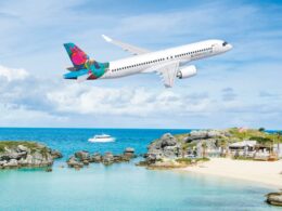 Airliner with a bright colorful tail flying over a tropical beach and rocky shoreline