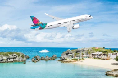 Airliner with a bright colorful tail flying over a tropical beach and rocky shoreline