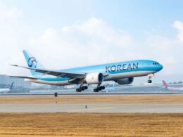 Korean Air jet lifting off from a runway with blue livery and tail logo visible against a clear sky airport in the background