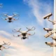 Quadcopter drones fly near a security camera tower against a blue sky at sunset