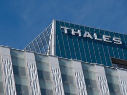 Modern glass office building with THALES signage on the roof against a clear blue sky
