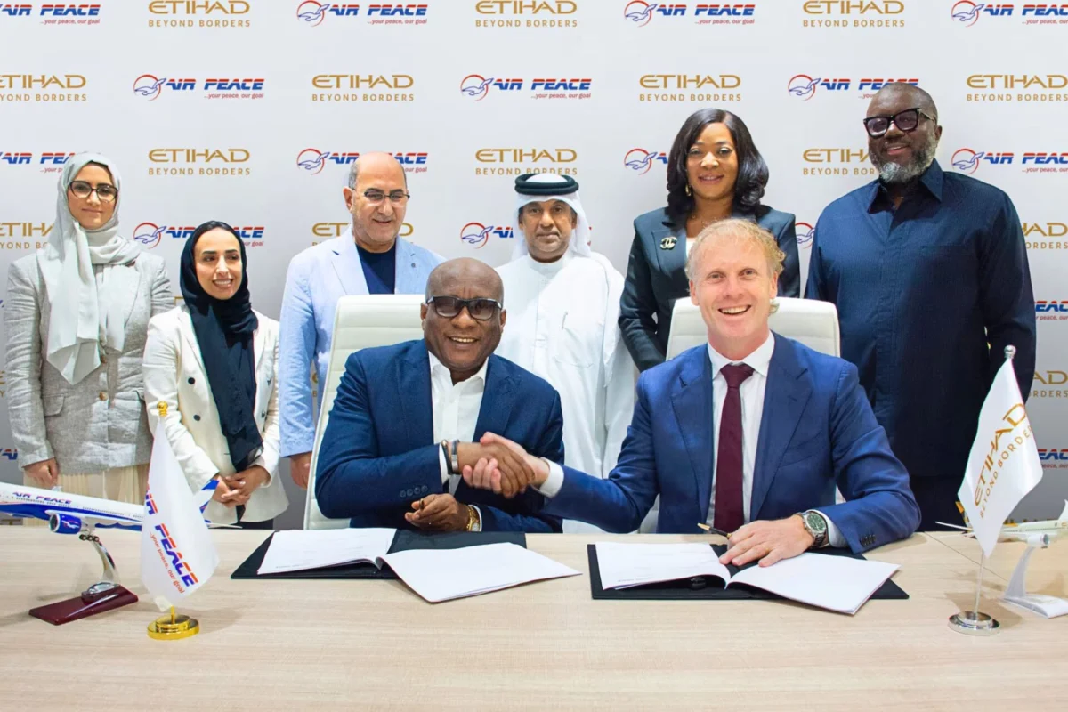 Etihad and Air Peace sign interline deal for connectivity Two men in suits shake hands over signed documents at a conference table surrounded by colleagues with Air Peace and Etihad logos in the backdrop