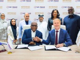 Two men in suits shake hands over signed documents at a conference table surrounded by colleagues with Air Peace and Etihad logos in the backdrop