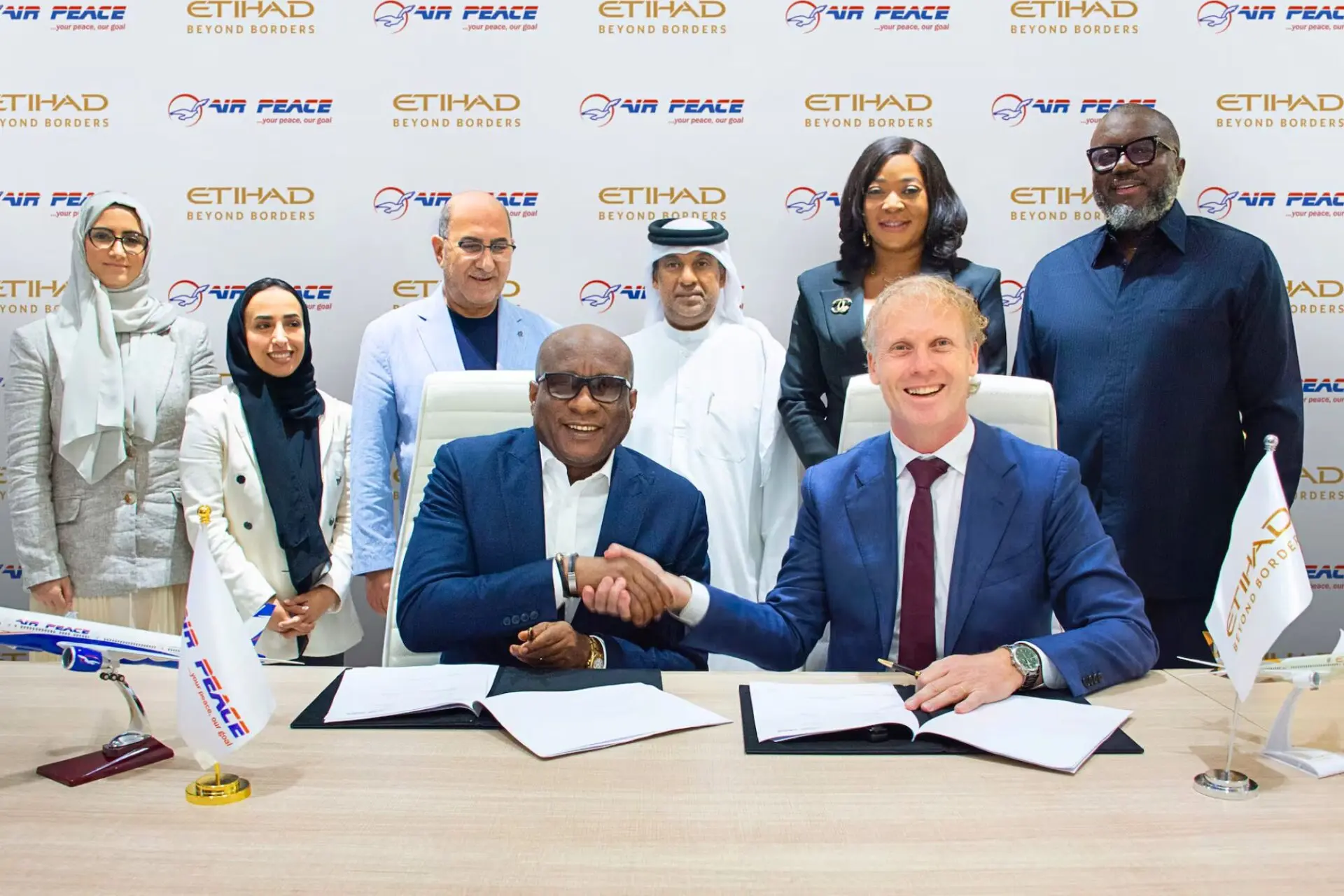 Two men in suits shake hands over signed documents at a conference table surrounded by colleagues with Air Peace and Etihad logos in the backdrop