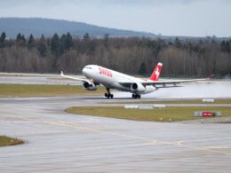 Swiss aircraft lifting off a rainy runway spray trailing from the wheels as it begins takeoff with forested hills in the background