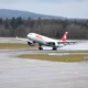 Swiss aircraft lifting off a rainy runway spray trailing from the wheels as it begins takeoff with forested hills in the background