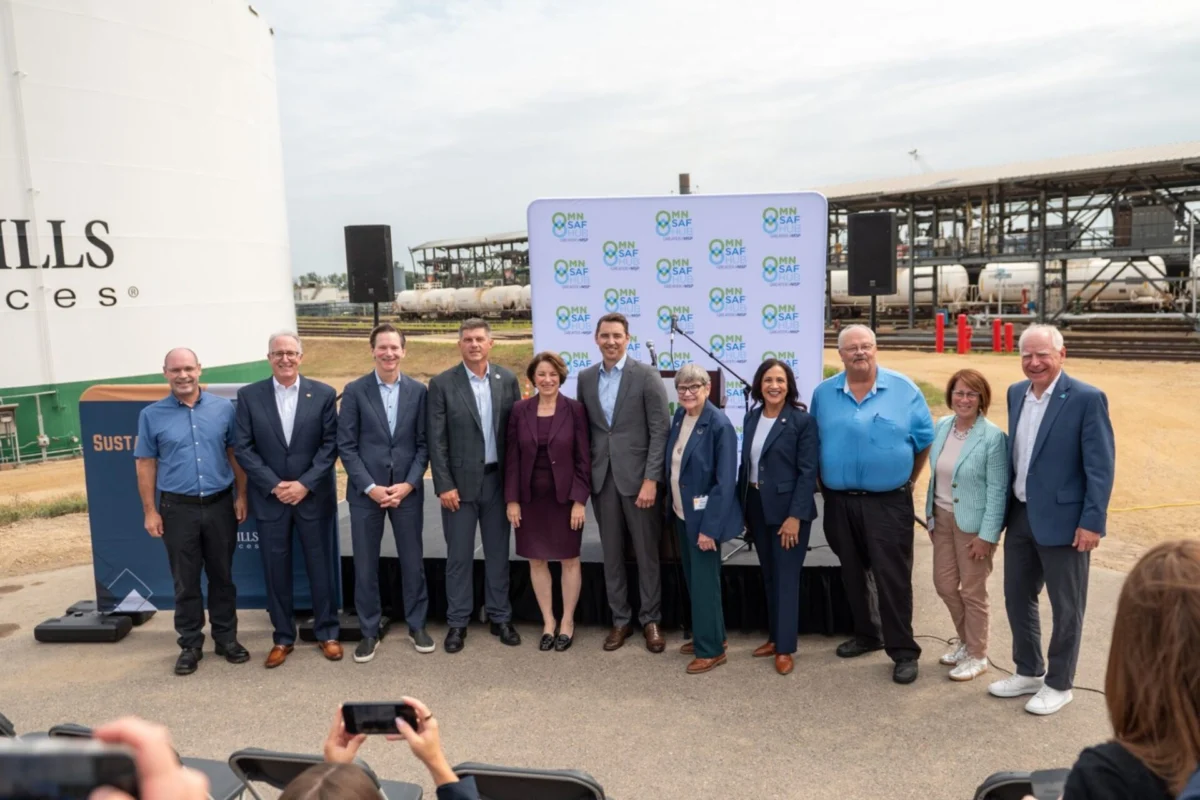 Group of ten professionals posing for a photo at an outdoor press event with a MN SAF Hub backdrop