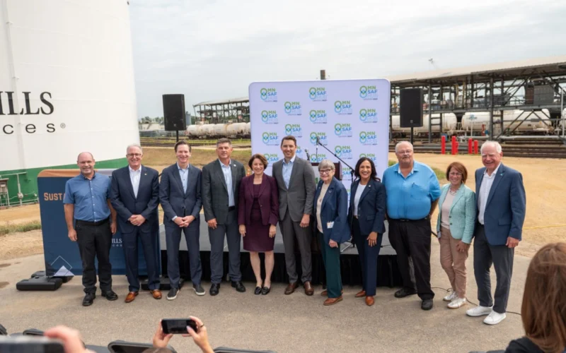 Group of ten professionals posing for a photo at an outdoor press event with a MN SAF Hub backdrop