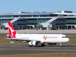 Australia Post aircraft with red tail at a modern airport terminal gate area
