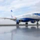 Airplane on a runway with blue nose and tail reflection visible on the wet tarmac under a cloudy sky