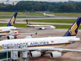 Singapore Airlines jets parked at a gate with blue and gold tail logos and a jet bridge in the foreground