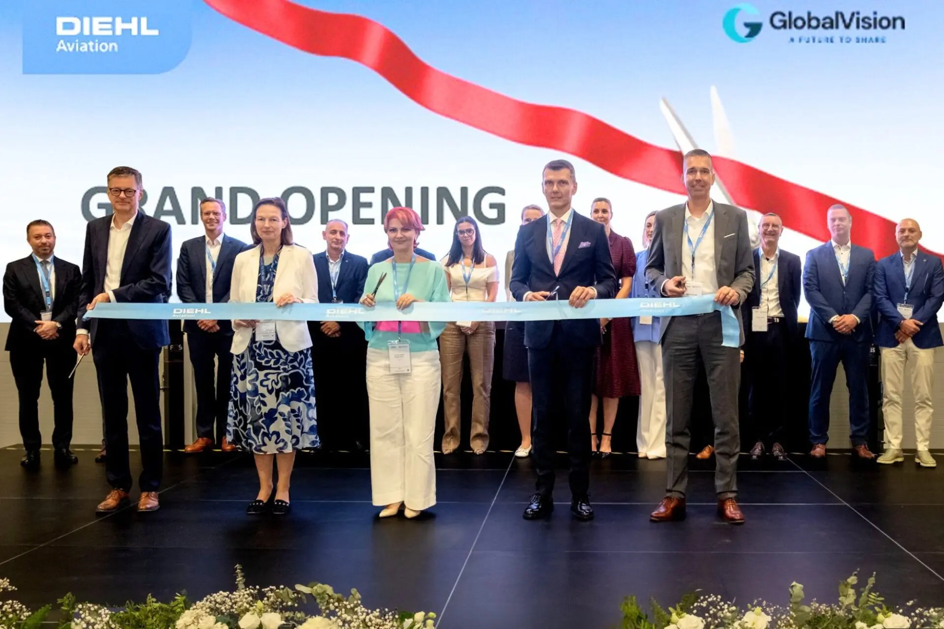 Group of professionals cutting a blue ribbon at a grand opening on a stage with DIEHL Aviation and GlobalVision logos in the background