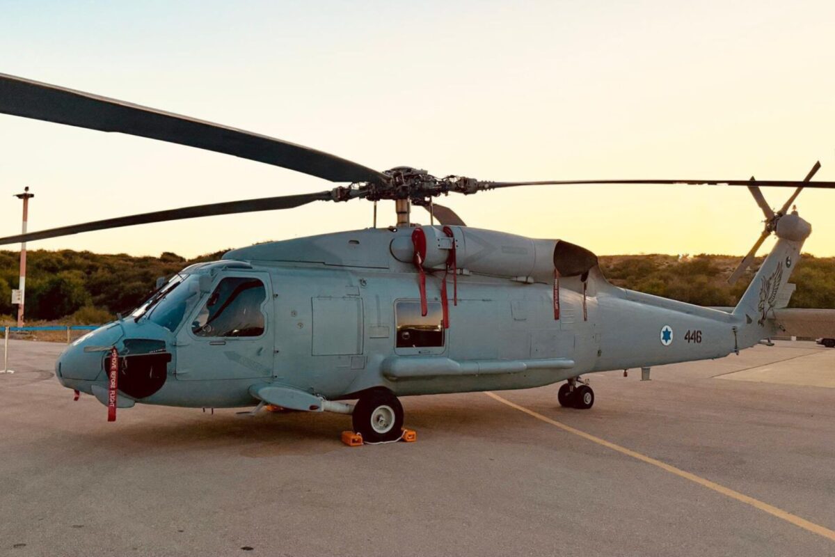 Side profile of a gray military helicopter parked on a tarmac at sunset rotor blades extended to the sides