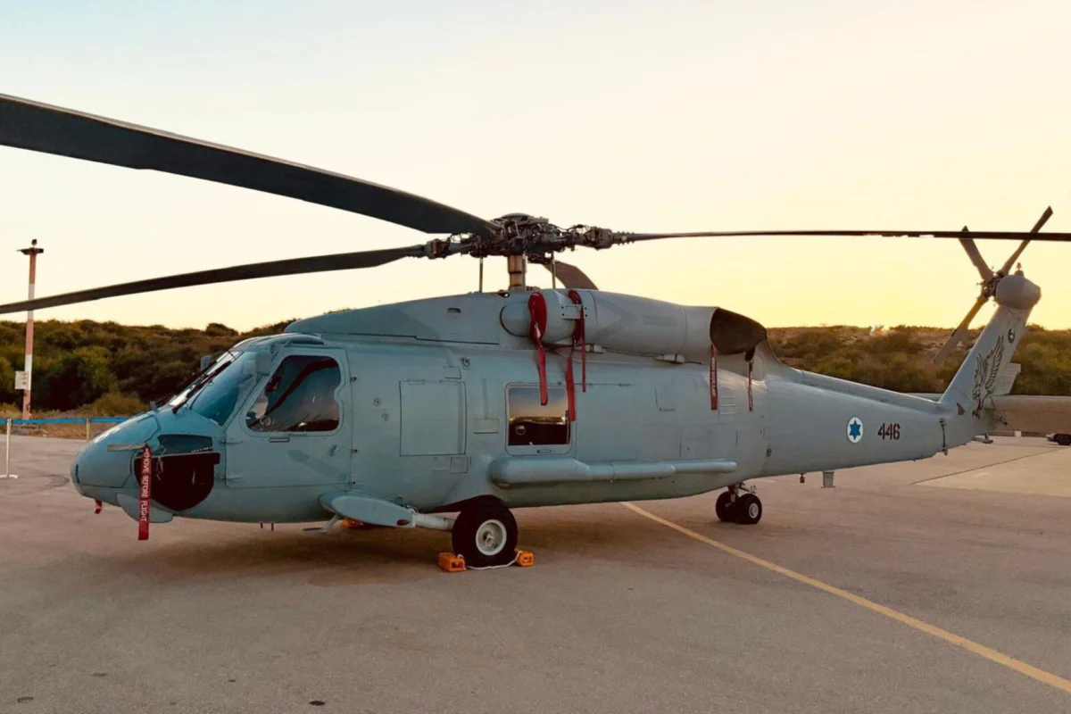 Side profile of a gray military helicopter parked on a tarmac at sunset rotor blades extended to the sides