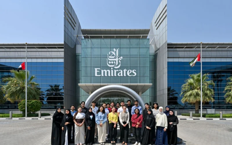 Group of diverse people posing for a photo in front of a modern Emirates building with glass facade and flags