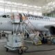Inside a large aircraft hangar a Lufthansa CityLine jet is being serviced with orange maintenance stairs and ground crews nearby in a bright open space