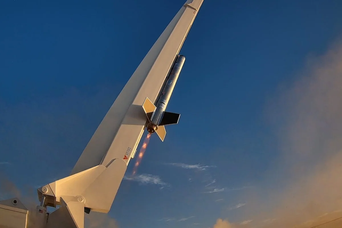 VenusAero RDRE Flight 01 Rocket mounted to a white aircraft tail during a test launch flames trailing from its engine against a blue sky