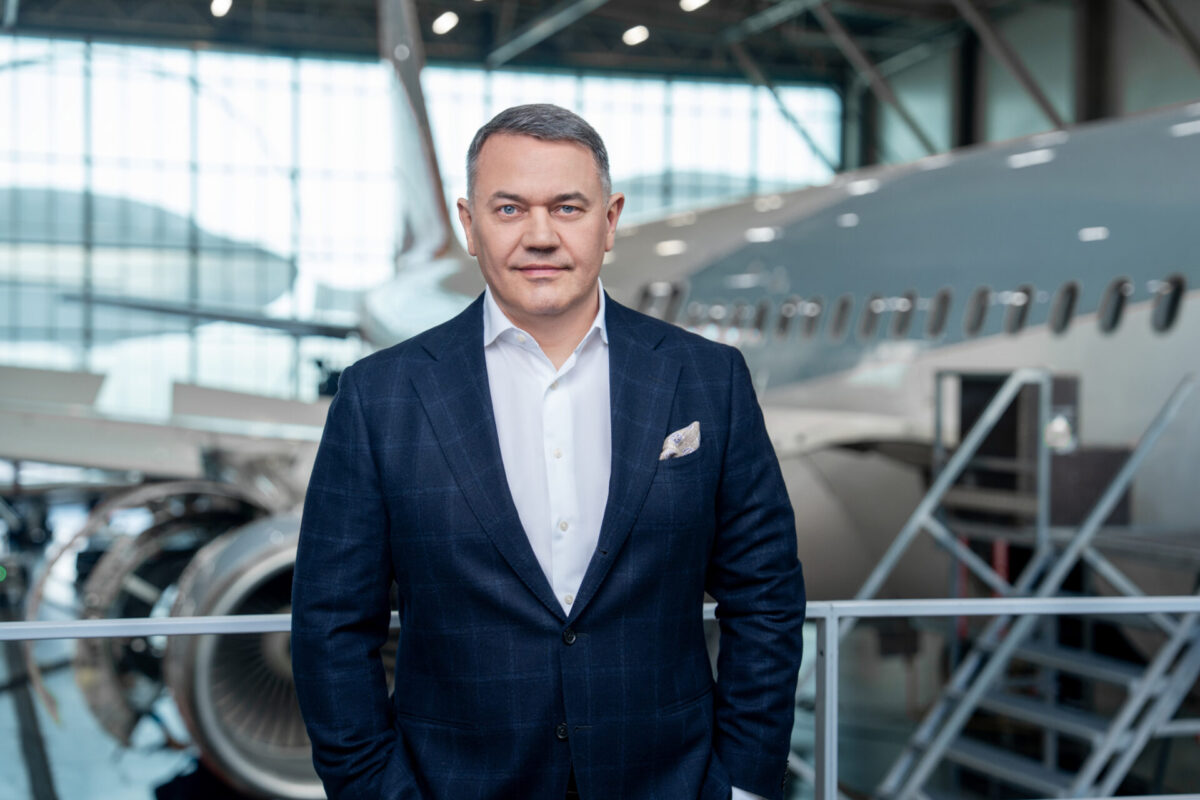 Zilvinas Lapinskas CEO of Avia Solutions Group Professional man in a dark blazer and white shirt standing in an aircraft hangar with a jet in the background