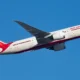 Air India aircraft in white and red livery flying against a clear blue sky angled upward